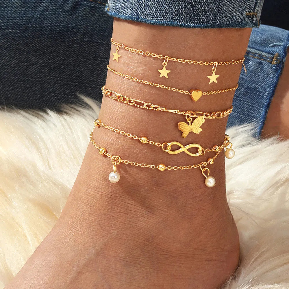 Four gold-tone alloy anklets with butterfly and heart pearl charms arranged as a set