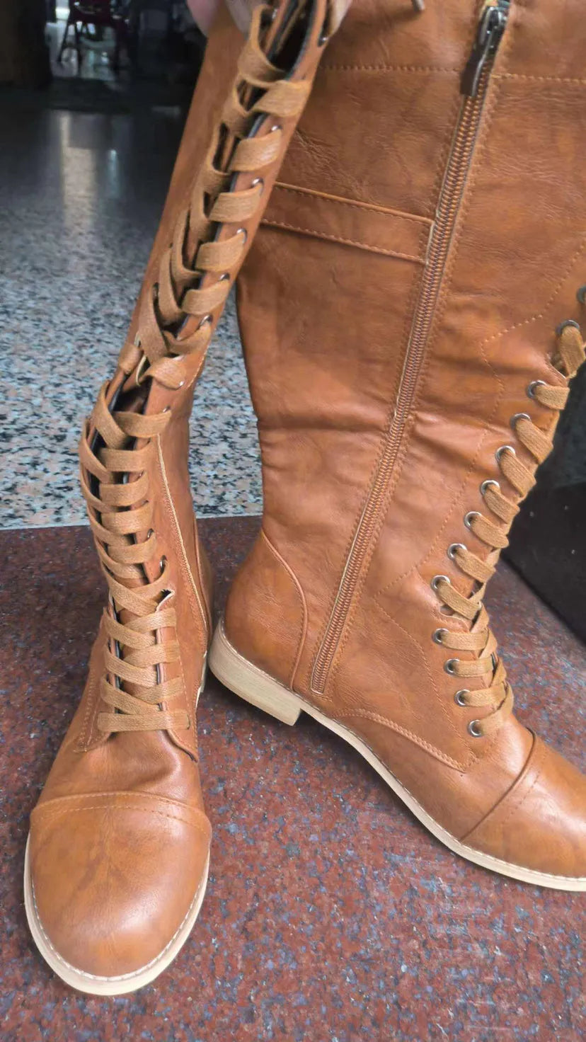 Women's black knee-high boots with a cross strap detail on the shaft, made of artificial PU leather.