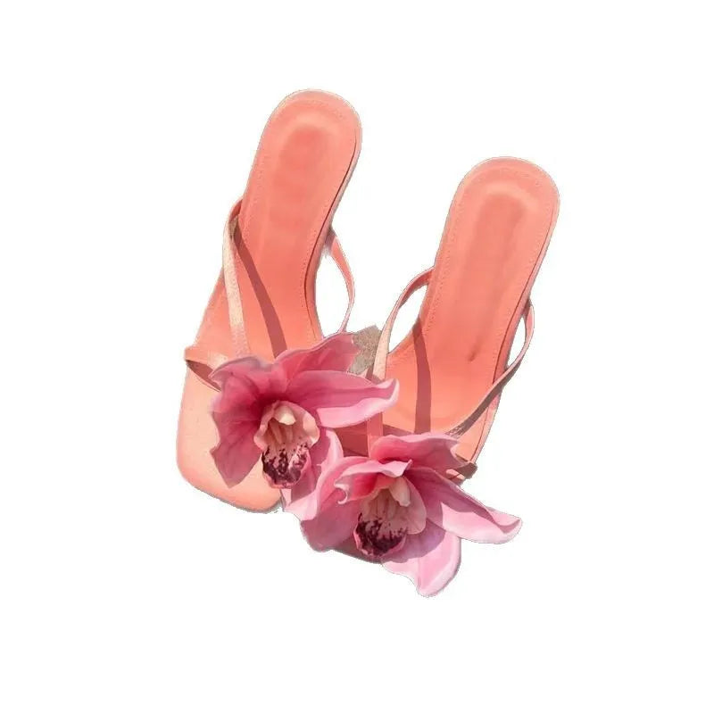 Pink women's sandals with a large artificial Phalaenopsis flower on the satin upper, a mid-heel, and a square toe.