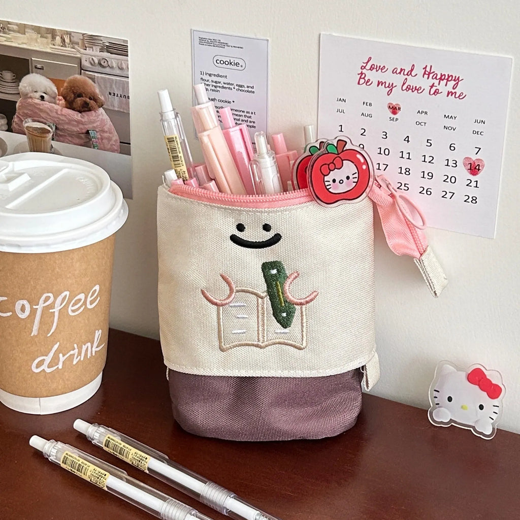 Brown collapsible Oxford cloth pencil case with zip, shown open next to pens and pencils.