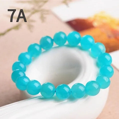 Natural blue-green Amazonite polished beads scattered on a surface, with a finished crystal bracelet.