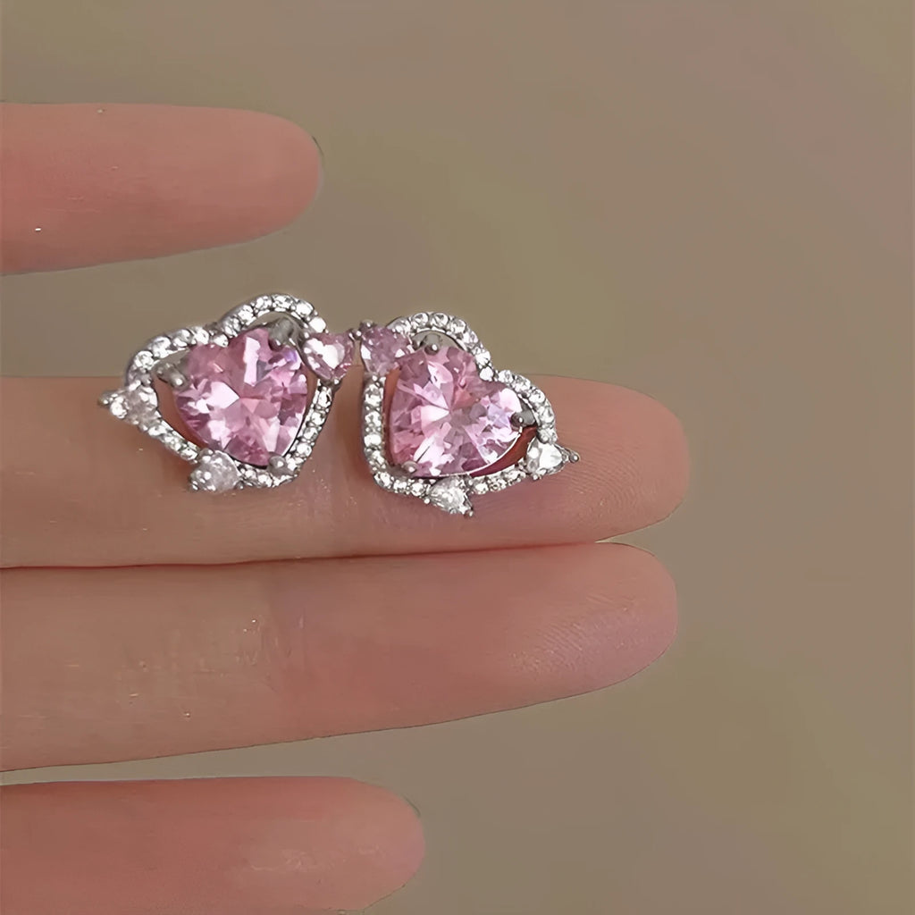 A pair of small white gold coloured heart shaped stud earrings for women on a jewellery card.