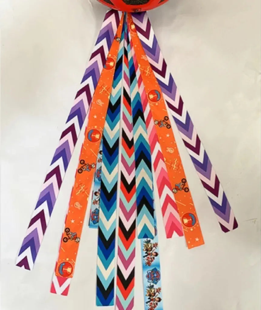 Colourful fabric helmet streamers for children's roller skating and ski helmets, shown in apricot, red, and grey.
