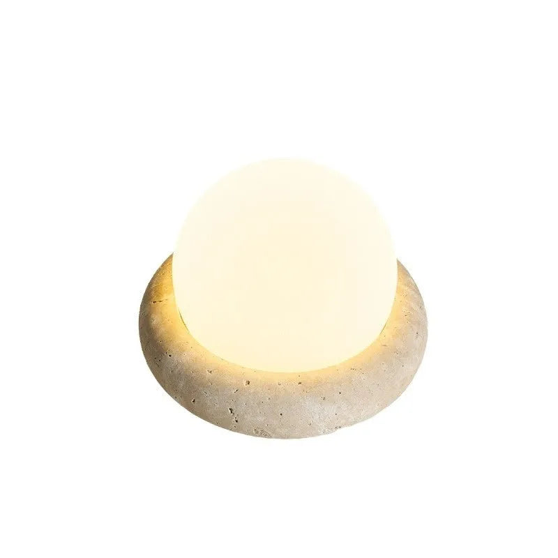 Cream coloured round rechargeable remote control night light on a bedside table.