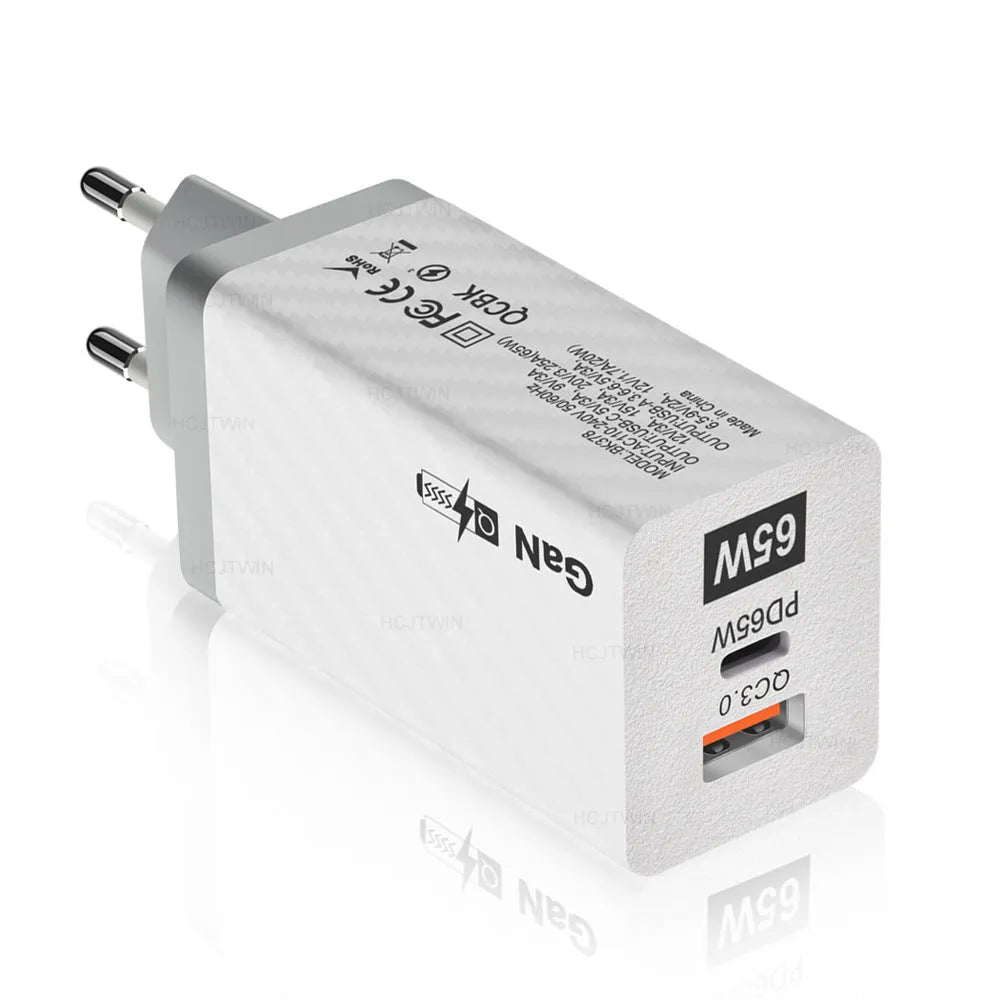 Compact black 65W GaN USB-C laptop charger with UK plug next to laptop