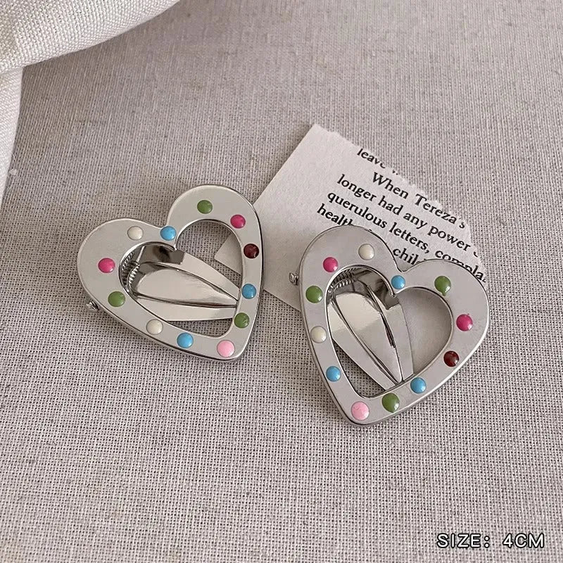 Two shiny silver metal duckbill barrettes with hollow star patterns on a plain background