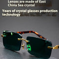A pair of dark green frameless crystal sunglasses with a gold-tone temple arm on a case.