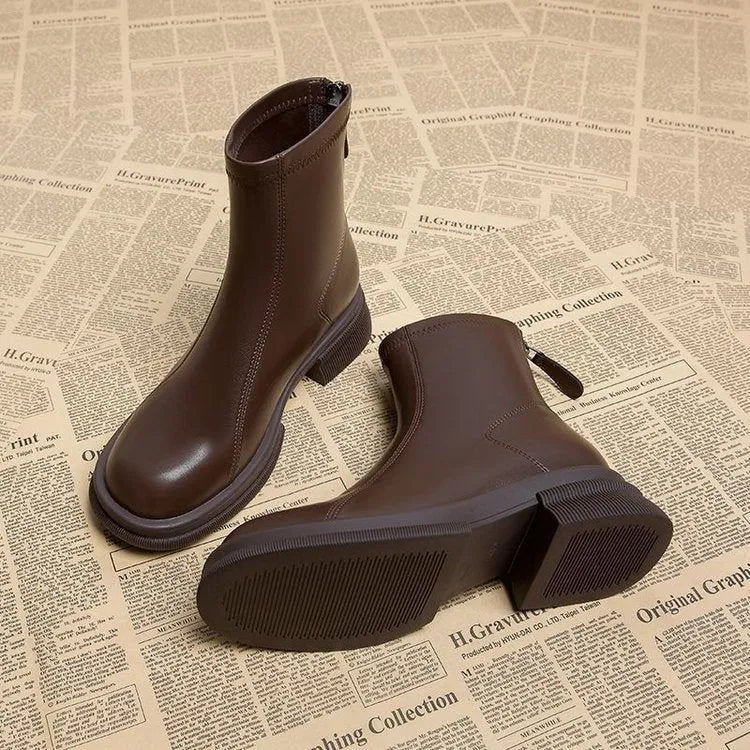Women's black ankle boot with flat heel and back zipper on a plain background.