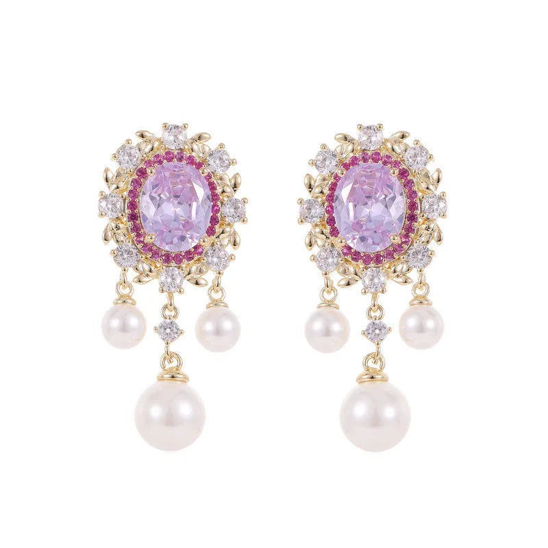 A pair of oval-shaped copper earrings with zircon inlay and a light-coloured pearl tassel.