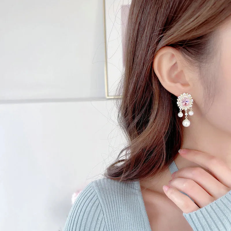 A pair of oval-shaped copper earrings with zircon inlay and a light-coloured pearl tassel.