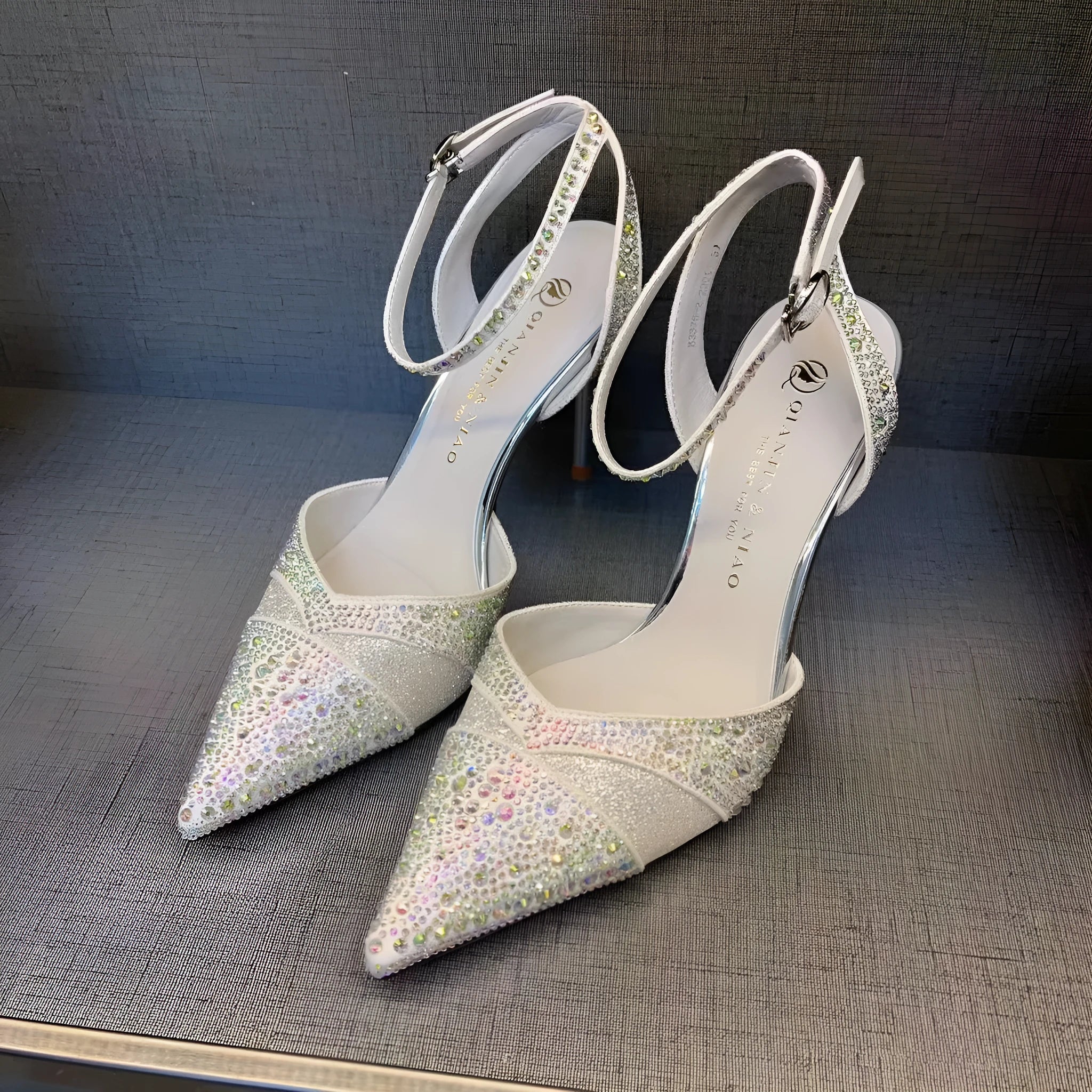 Women's silver high heel shoe with stiletto heel, pointed toe, and red sole on a white background.